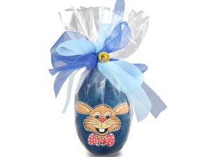 Uovo di Pasqua blu decorato con fiocchi, campanelli e un coniglio, su sfondo bianco